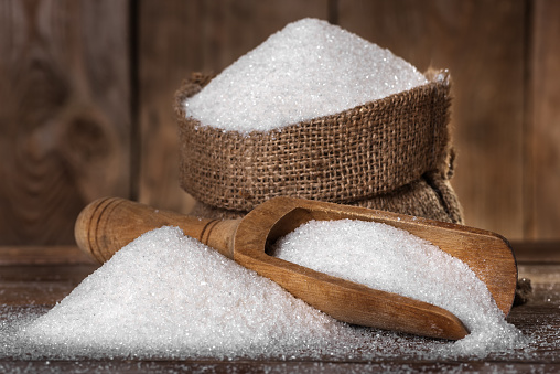 The sugar in a bag and spoon close-up on the old wooden background